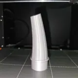 Szary lejek, wydrukowany na drukarce 3D, stoi na platformie roboczej.