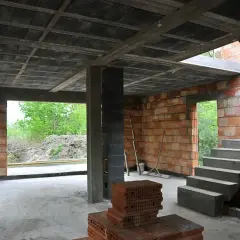 Budowa domu w stanie surowym. Widać strop ackermana, schody, ściany z pustaków i cegieł.
