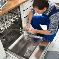 Technik w niebieskim kombinezonie pokazuje, jak podłączyć zmywarkę, pracując przy otwartych drzwiach urządzenia.
