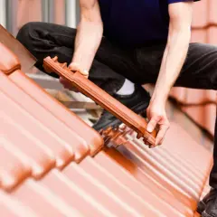 Dachówka ceramiczna układana na dachu. Widać ręce mężczyzny montującego dachówkę, uwzględniając odpowiedni kąt nachylenia dachu.