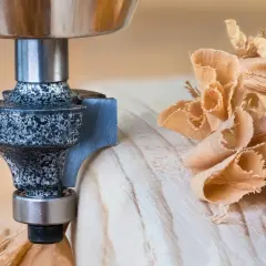 Frez do drewna tworzy ozdobne krawędzie, a wokół unoszą się delikatne wióry.
