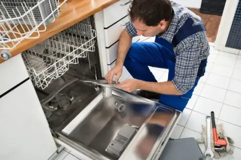 Technik w niebieskim kombinezonie pokazuje, jak podłączyć zmywarkę, pracując przy otwartych drzwiach urządzenia.