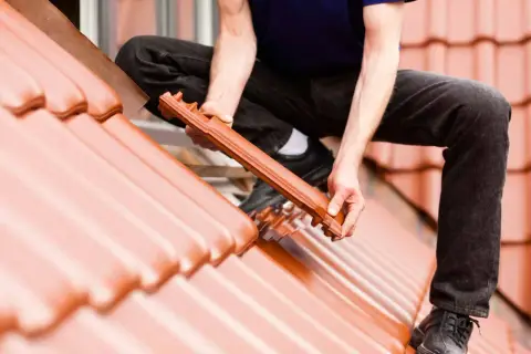 Dachówka ceramiczna układana na dachu. Widać ręce mężczyzny montującego dachówkę, uwzględniając odpowiedni kąt nachylenia dachu.