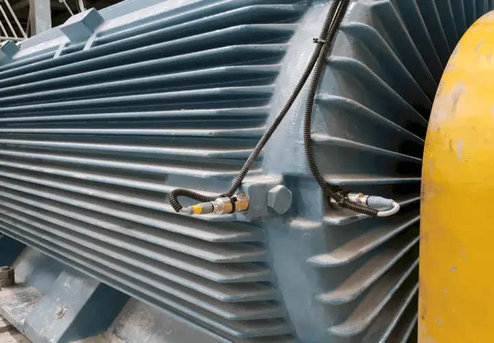 Duży, niebieski silnik przemysłowy z czujnikami wibracji. Obok żółty element, być może obudowa lub inny mimośród.