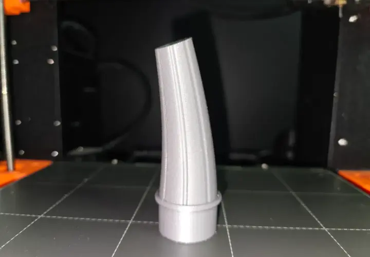 Szary lejek, wydrukowany na drukarce 3D, stoi na platformie roboczej.
