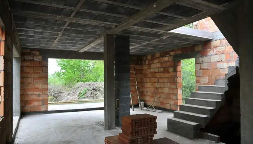 Budowa domu w stanie surowym. Widać strop ackermana, schody, ściany z pustaków i cegieł.