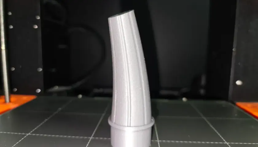 Szary lejek, wydrukowany na drukarce 3D, stoi na platformie roboczej.