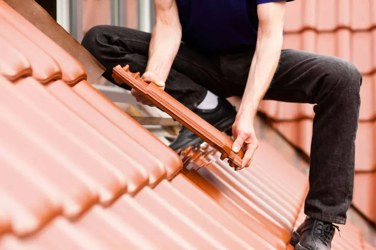 Dachówka ceramiczna układana na dachu. Widać ręce mężczyzny montującego dachówkę, uwzględniając odpowiedni kąt nachylenia dachu.